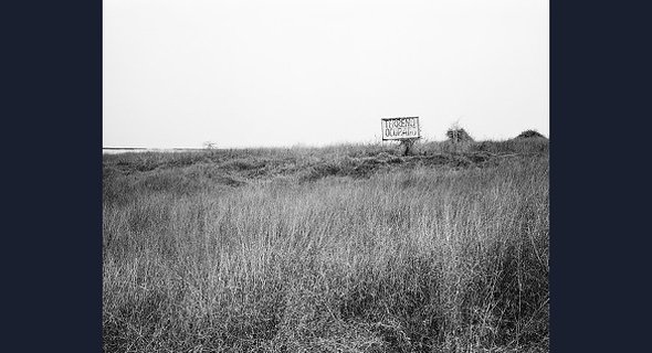 This coarse, grassy landscape appears at first glance to be empty, yet the billboard declaring "Terreno Ocupado" – Portuguese for "occupied land" – reveals this site in Luanda as both active and politically charged.